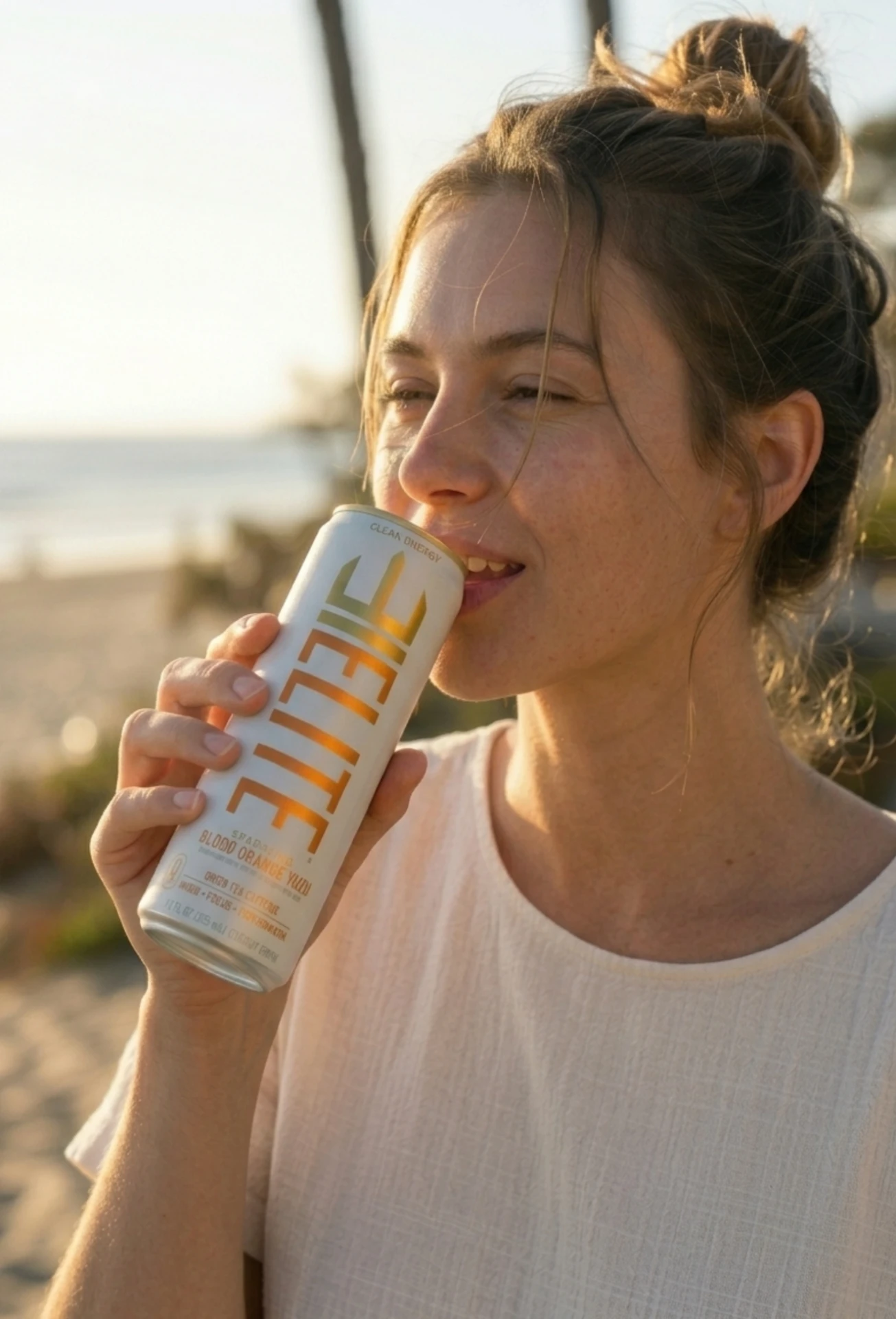Woman sipping an ELITE Blood Orange Yuzu can at golden hour on the beach